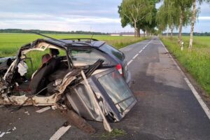 Unfallstelle mit beschädigtem Auto und mehreren Straßenbäumen, Rettungskräfte vor Ort.