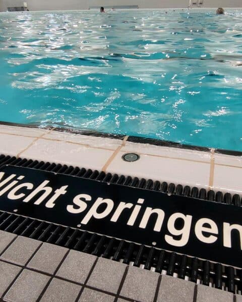 Ein Schwimmbad mit Kindern, Sicherheitsvorkehrungen sowie ein Hinweis auf Schwimmabzeichen.