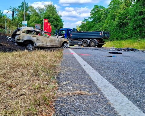 Schwerer Verkehrsunfall: brennendes Auto, Feuerwehr im Einsatz, gesperrte Straße, traurige Unfallstelle.