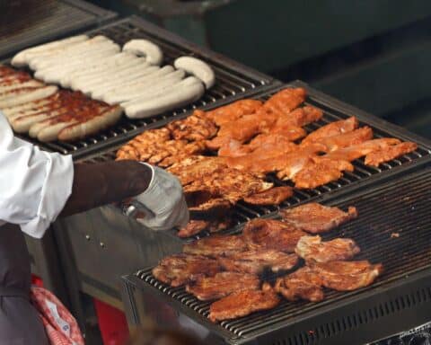 Gegrillte Hähnchenschnitzel und Würste symbolisieren steigenden Fleischkonsum und Umweltbelastungen.