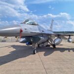 F-16 Kampfjet vor Militärhintergrund, symbolisiert zeitgemäße Verteidigung und geopolitische Herausforderungen.