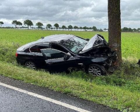 Verunfallter BMW neben einem Straßenbaum, Polizei und Rettungsdienst vor Ort.