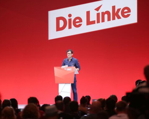 Luigi Pantisano spricht auf einer politischen Veranstaltung, umgeben von Journalisten und Mikrofonen.