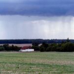 Dunkle Gewitterwolken über einem Acker, drohender Regen und stürmische Böen im Hintergrund.