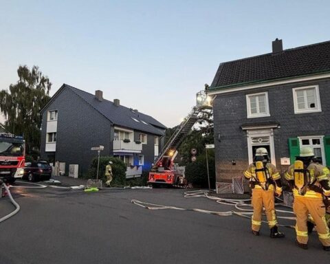 Feuerwehrlöscharbeiten an einem Wohngebäude, Haus im Hintergrund, Einsatzkräfte mit Atemschutz.