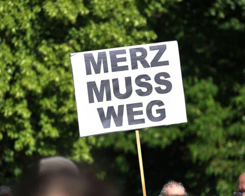 Kundgebung gegen Kanzler Merz, Protestplakate, Redner auf Bühne, engagierte Teilnehmer in Dresden.