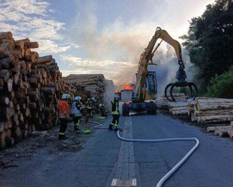 Brennender Bagger auf einem Gelände, Feuerwehr im Einsatz, Rettungsdienste und Polizei anwesend.