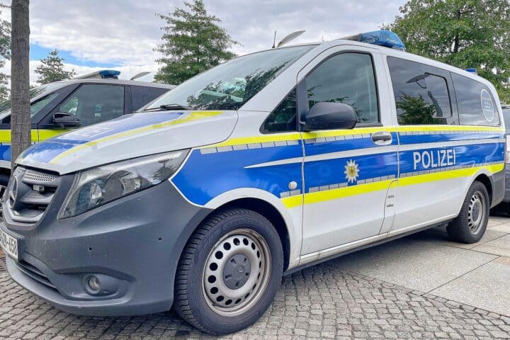 Polizeiauto vor Mehrfamilienhaus mit Einsatzkräften, dramatische Situation nach Bedrohung mit Schusswaffe.