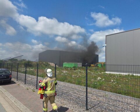 Rauchentwicklung aus Lagerhalle, Feuerwehr im Einsatz, Brandbekämpfung und Bevölkerungswarnung sichtbar.