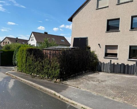Feuerwehr löscht Heckenbrand, Einsatzkräfte an der Brandstelle, keine Verletzten, Straße gesperrt.