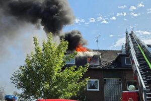Ein Mehrfamilienhaus-Dachstuhl steht in Vollbrand; Feuerwehr im Einsatz, Drehleiter und Einsatzkräfte vor Ort.