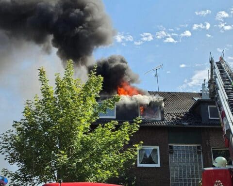 Ein Mehrfamilienhaus-Dachstuhl steht in Vollbrand; Feuerwehr im Einsatz, Drehleiter und Einsatzkräfte vor Ort.