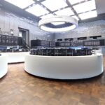Dax zeigt Rückgang, Börsensaal mit Aktientafeln und Marktteilnehmern im Hintergrund.