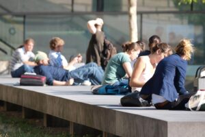 Junge Studierende vor einer Universität, Fokus auf Wohnkostenbelastung und Einkommen.