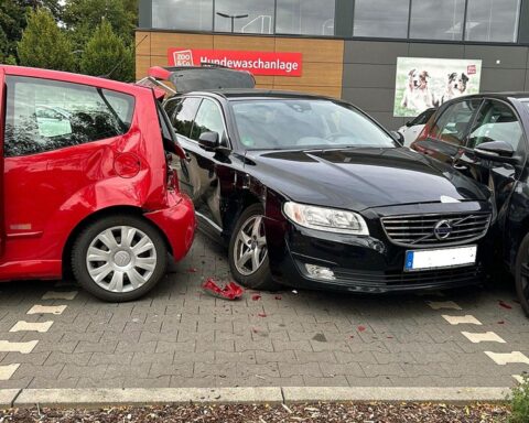 Verkehrsunfall auf Supermarktparkplatz: umgestoßene Mutter, rückwärts fahrender Citroën, Polizei und Rettungskräfte.