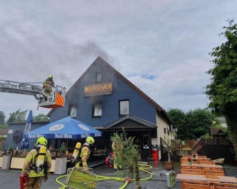 Dichter Rauch dringt aus einem Gebäude, Feuerwehr kämpft gegen den Brand mit Drehleiter.