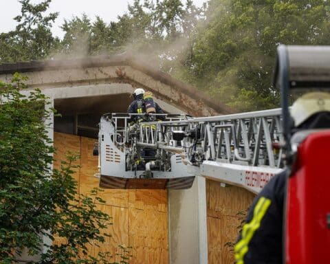 Feuerwehrleute löschen Brand in ehemaligem Schulgebäude, Rauch dringt aus einem Fenster.