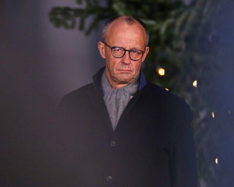 Friedrich Merz beim Weihnachtsbaumschlagen, Ausdruck von Anstrengung und Unbehagen sichtbar.