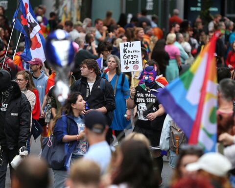 Parade mit bunten Fahnen, fröhlichen Menschen, die für queere Rechte und Schutz demonstrieren.