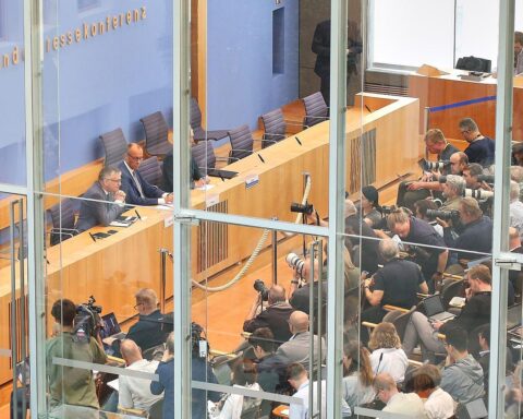 Friedrich Merz auf Sommerpressekonferenz, umgeben von Journalisten und Kameras.