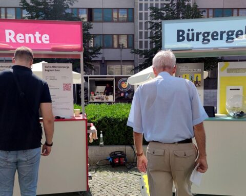 Passanten vor Infoständen zu Rente und Bürgergeld; Sozialhilfeausgaben in NRW steigen moderat 2025.