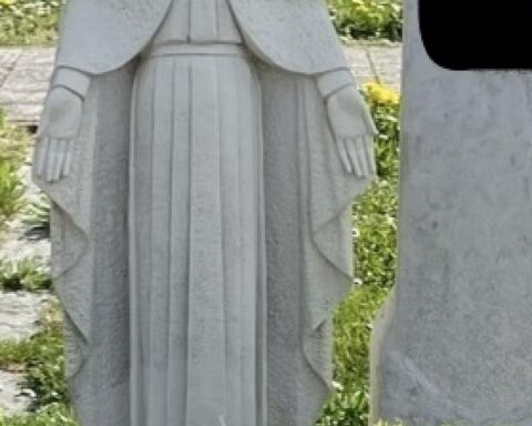 Eine entwendete Madonna-Statue auf einem Friedhof, umgeben von Grabsteinen und Trauer.