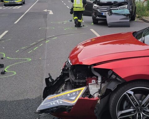 Ein Unfallfahrzeug auf der Straße, Feuerwehr im Einsatz, verletzter Fahrer wird gerettet.