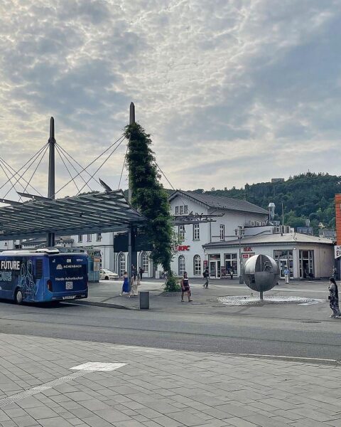 Bushaltestelle in Siegen (ZOB) bei wechselhaftem Wetter, Wolken und leichter Regen im Hintergrund.