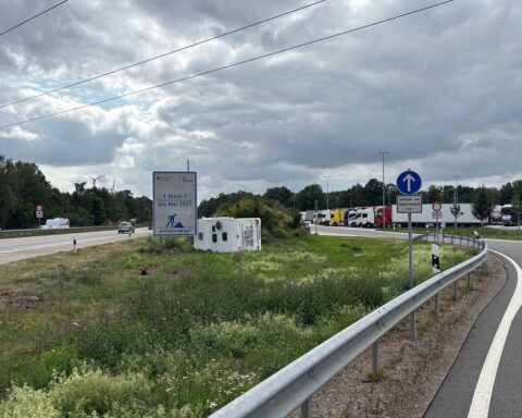 Ein verunfalltes Wohnmobil liegt auf der Seite zwischen Autobahn und Parkplatz; Einsatzkräfte am Unfallort.